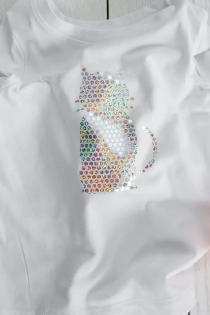 transferring Cricut Holographic Mosaic Iron On  in a cat shape to a white shirt