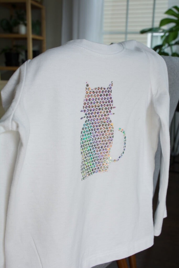 transferring Cricut Holographic Mosaic Iron On  in a cat shape to a white shirt