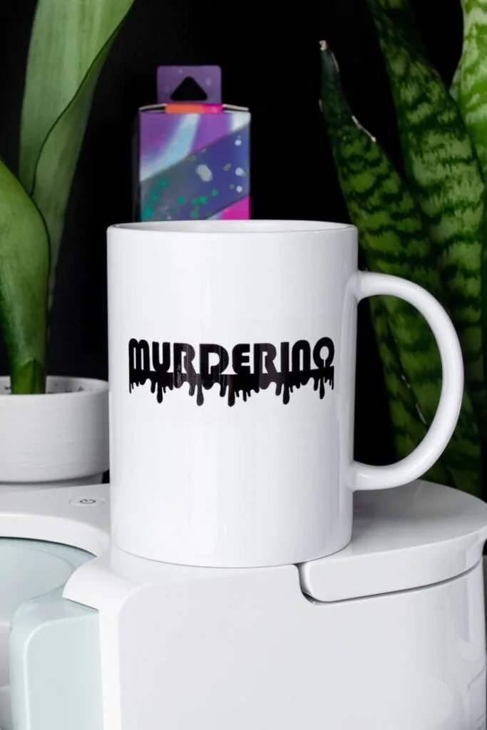 mug that says murderino sitting on top of a Cricut mug press
