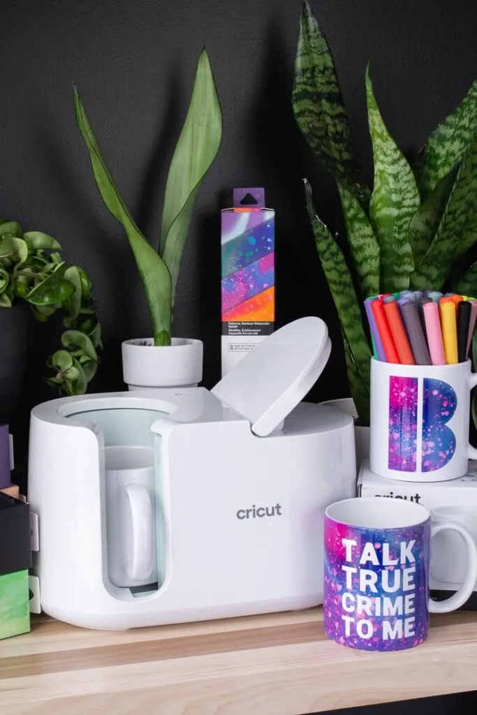 Cricut mug press, mugs, Infusible Ink transfer sheets, and plants on a table