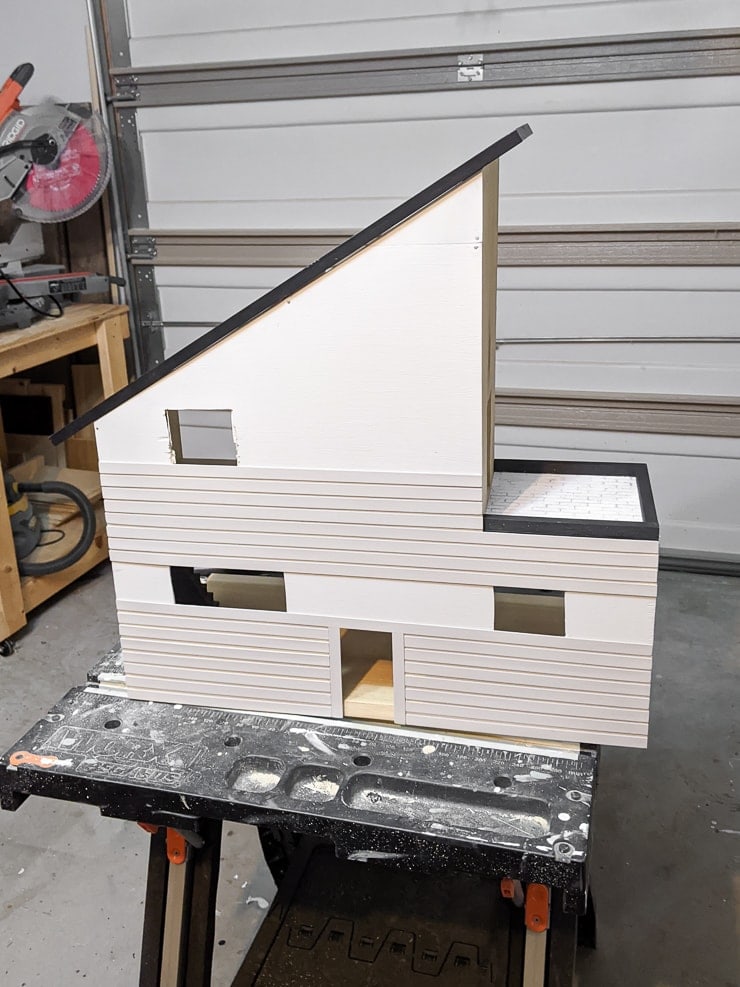 adding painted pieces of balsa wood to the dollhouse using wood glue and painter's tape