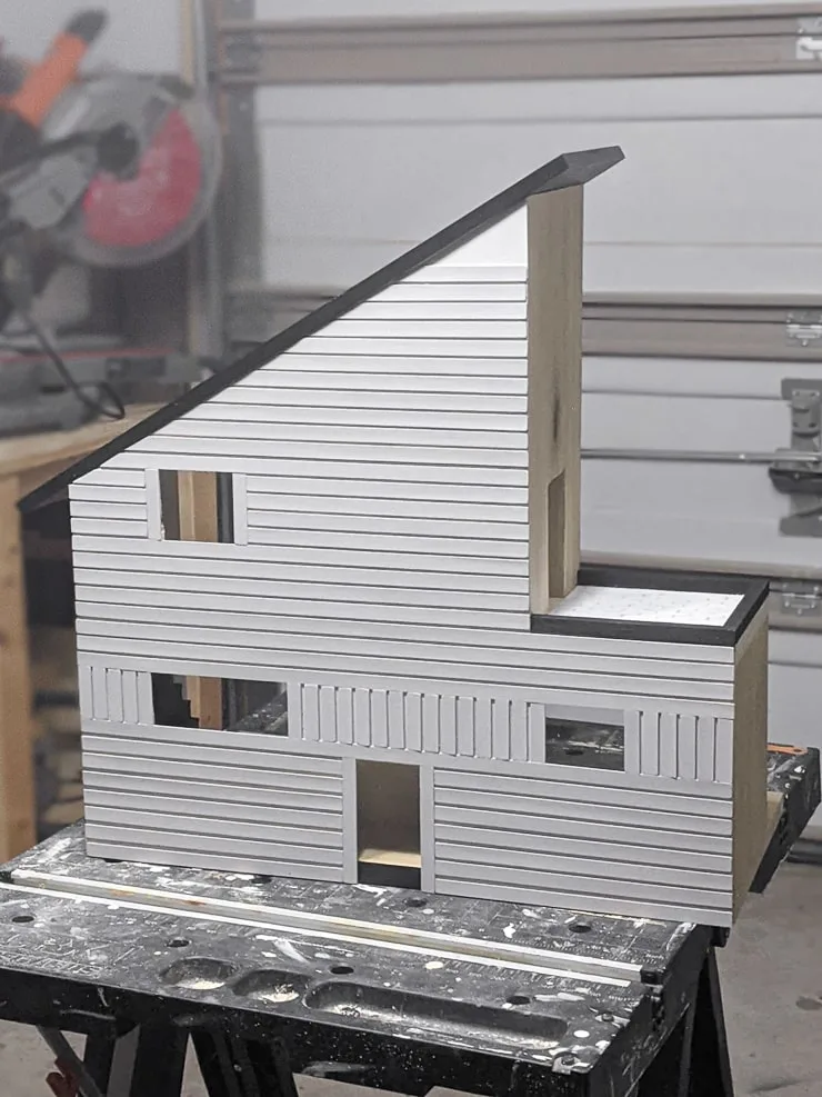 adding painted pieces of balsa wood to the dollhouse using wood glue and painter's tape
