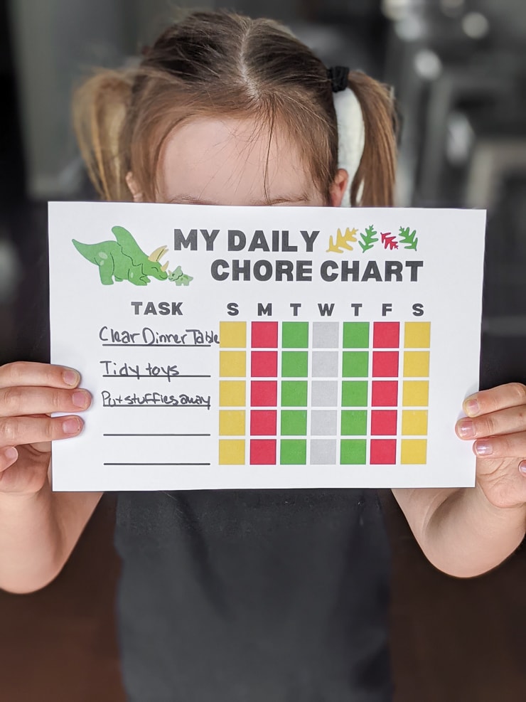 little girl holding a dinosaur-themed daily chore chart