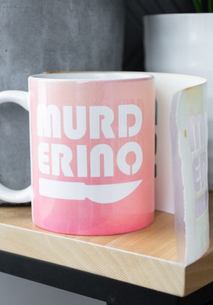 removing an Infusible Ink transfer sheet from a mug that says "murderino" created with a Cricut Mug Press