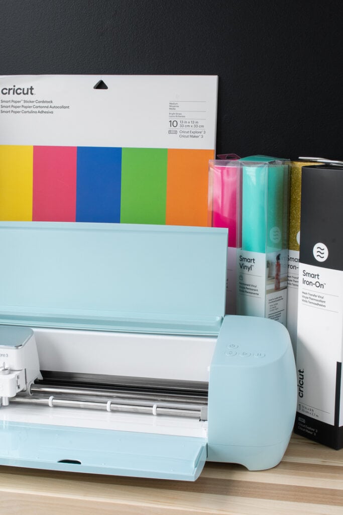 Cricut Explore 3 machine on a table with a pack of smart paper sticker cardstock and vinyl