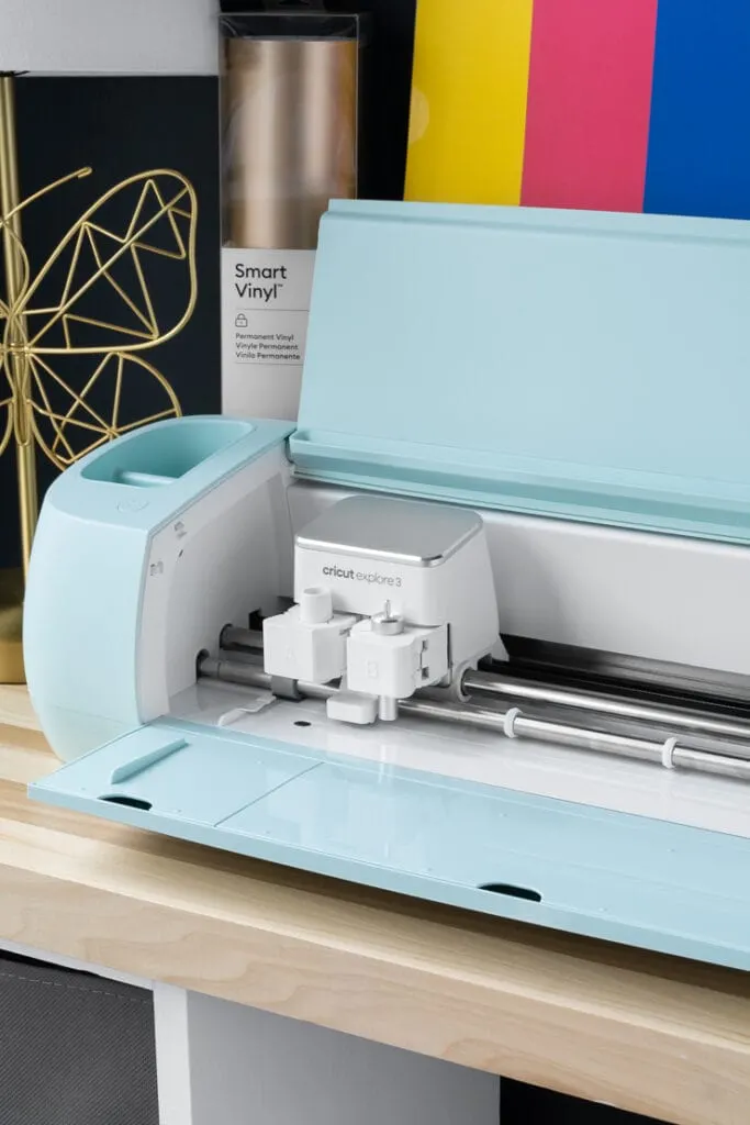 Cricut Explore 3 machine on a table with a pack of smart paper sticker cardstock and vinyl