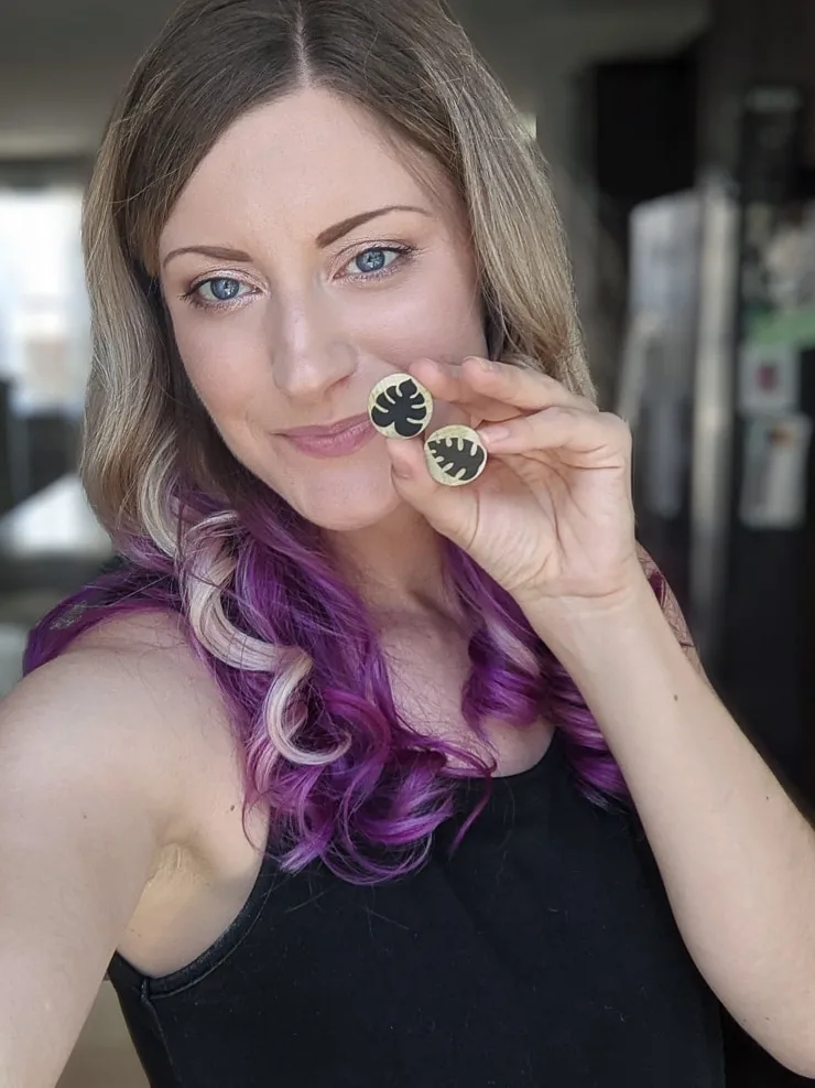 woman with purple hair holding two small magnets with vinyl leaf decals on them