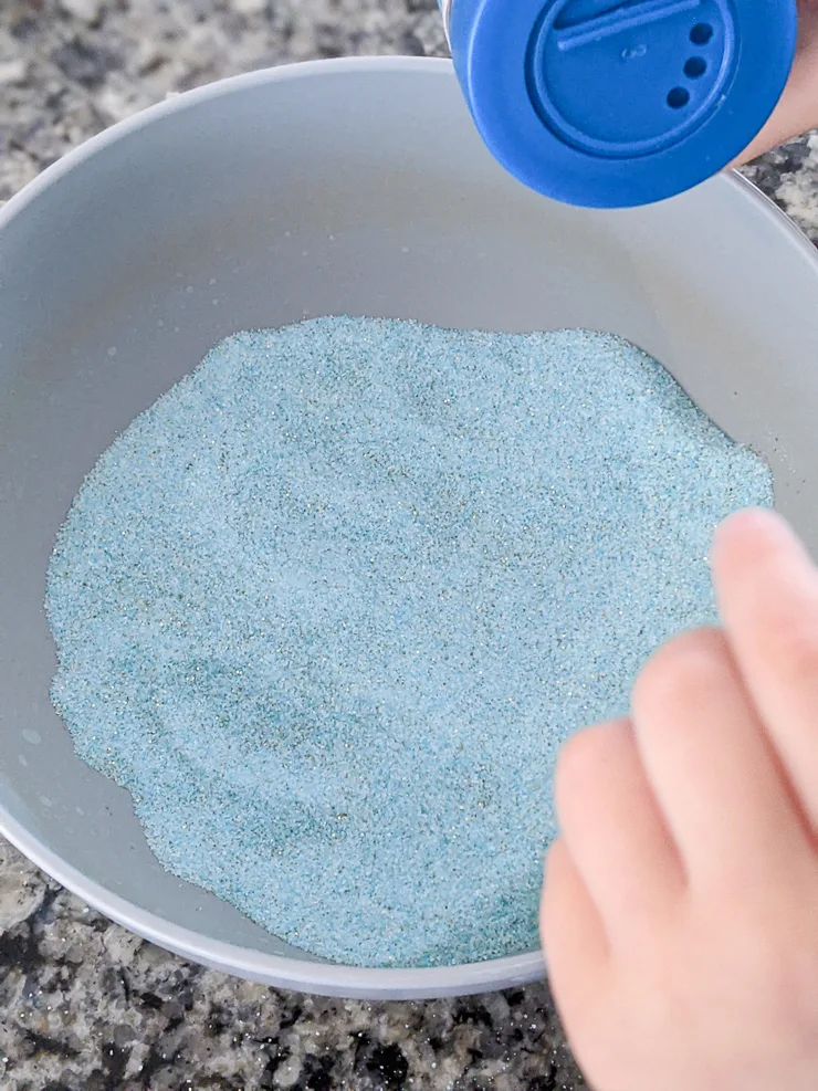 mixing blue sand and glitter in a bowl