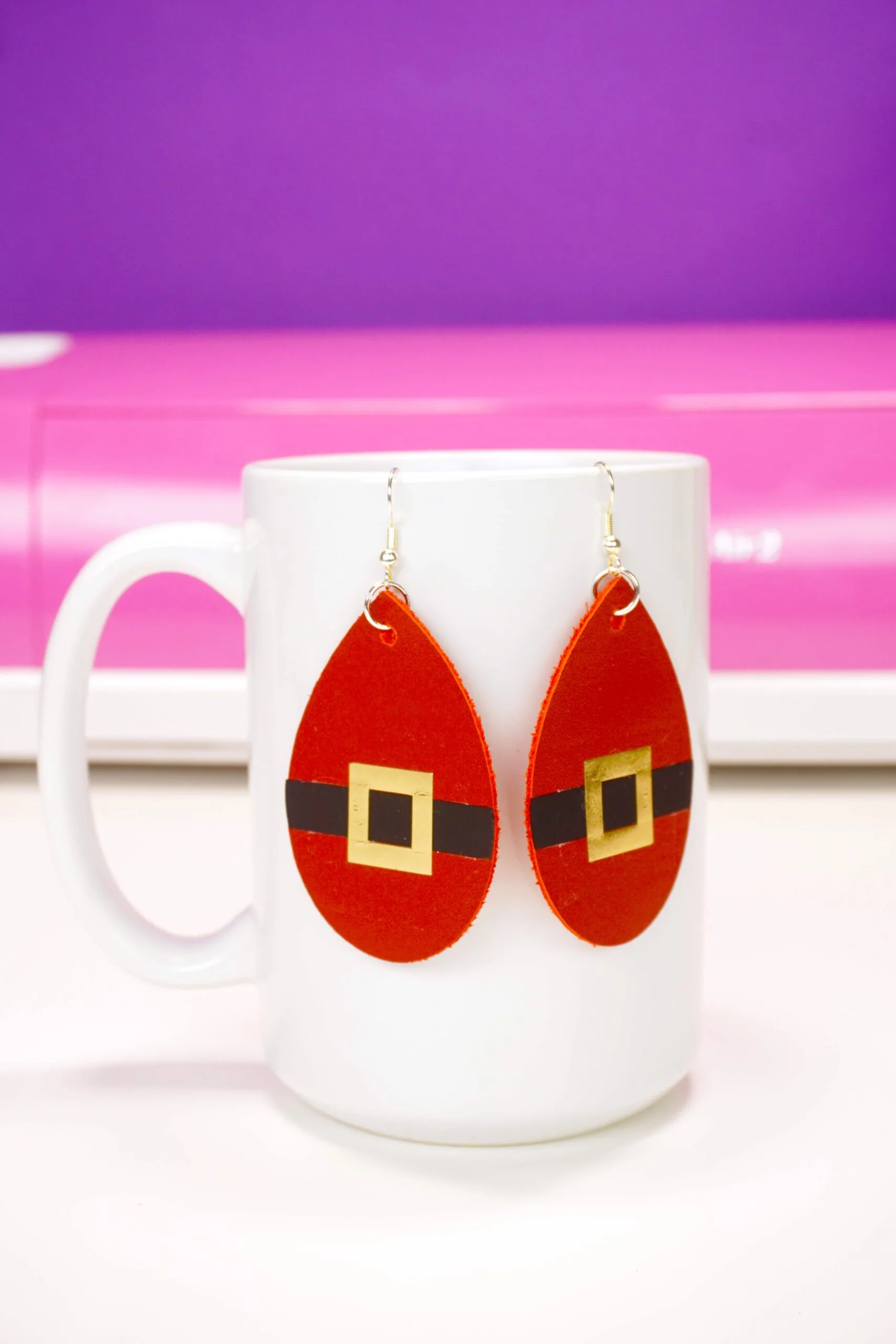 santa suit earrings hanging on white mug