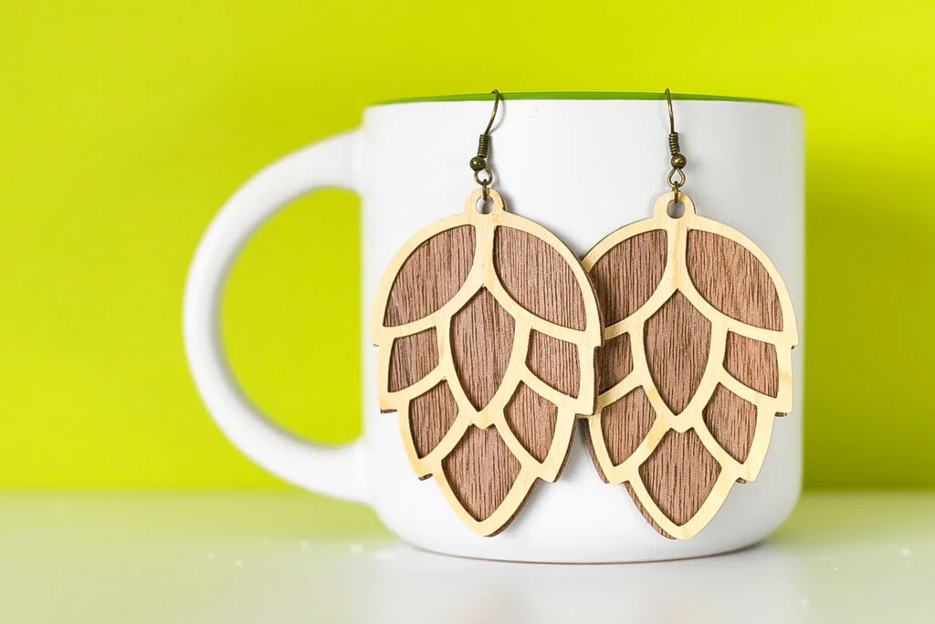 pinecone earrings made from wood veneer hanging on a white mug