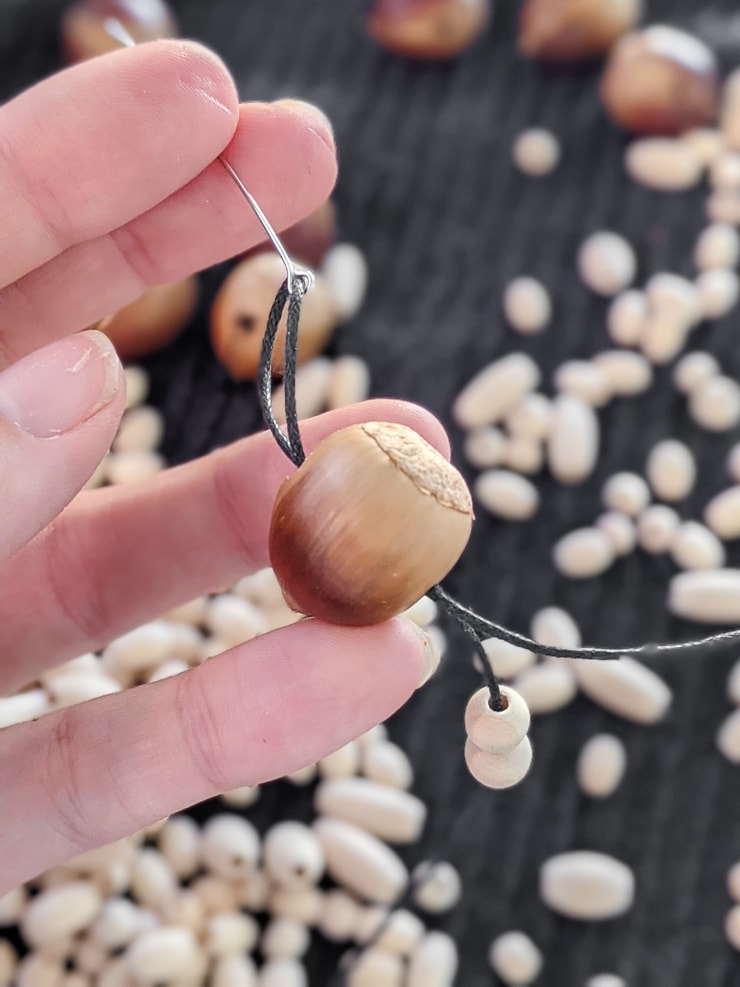 threading acorns onto a string to make a DIY fall garland