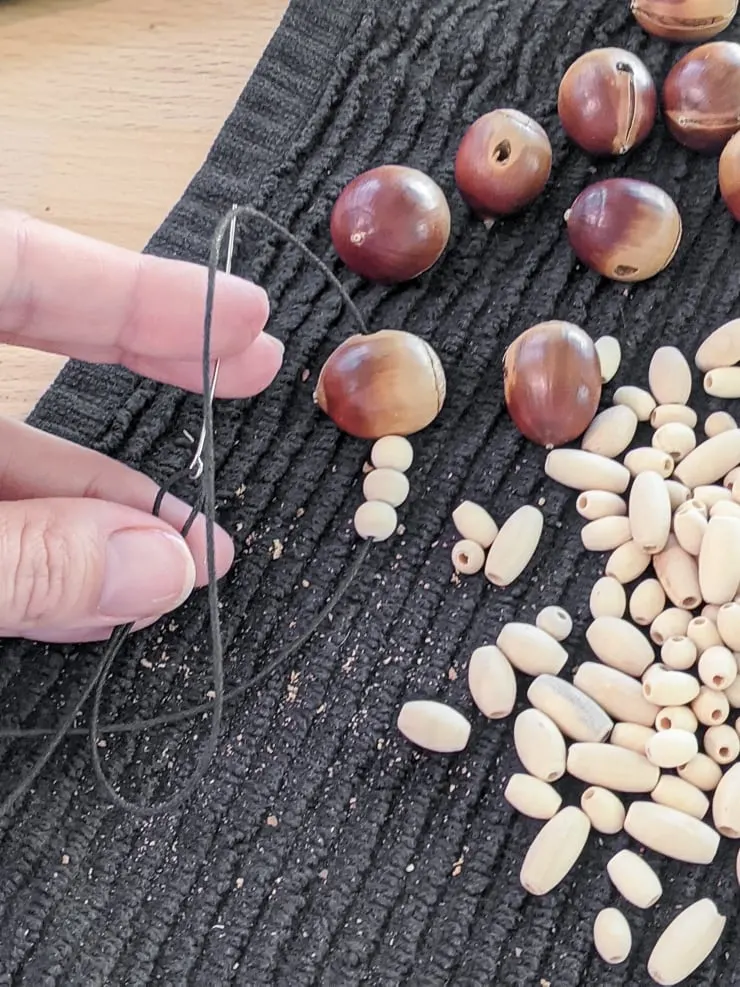 threading acorns and wood beads onto a string to make a DIY fall garland