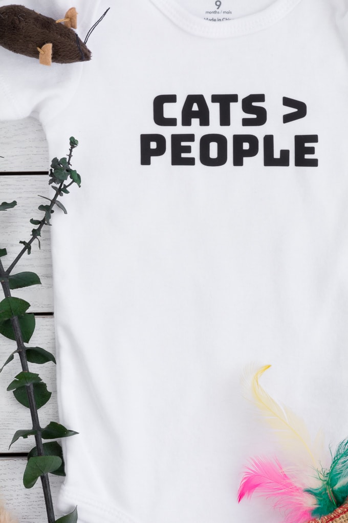 baby bodysuit that says cats > people in black iron-on