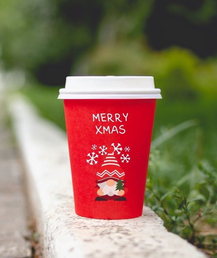 red disposable coffee cup that says MERRY XMAS and has a gnome on it