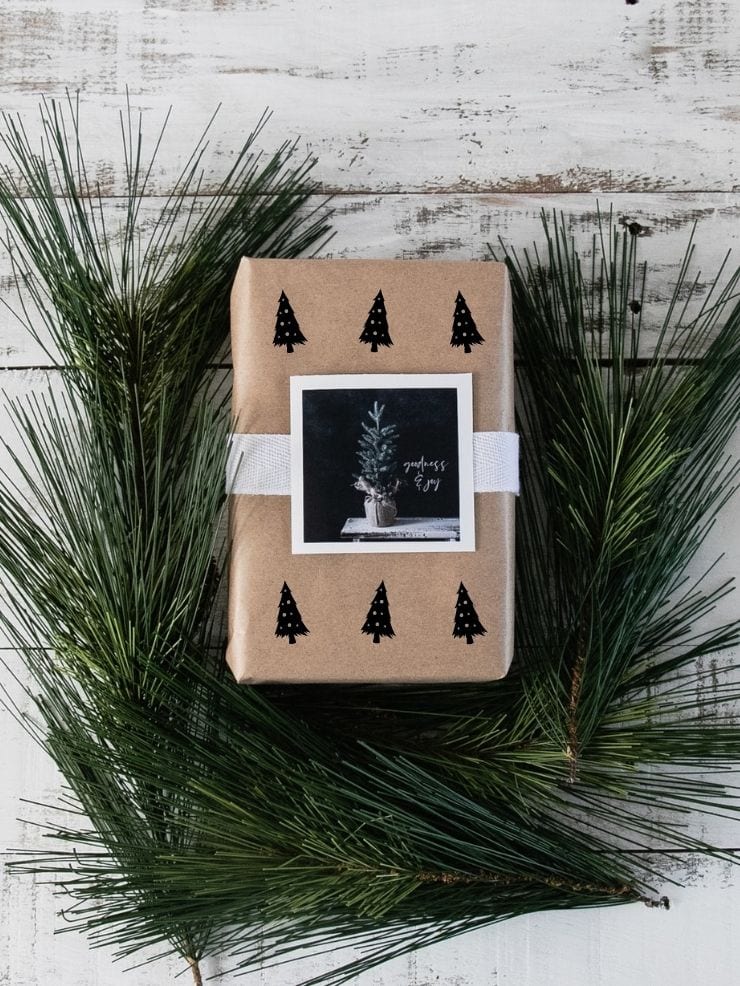 brown paper package with Christmas trees on it laying on pine needles