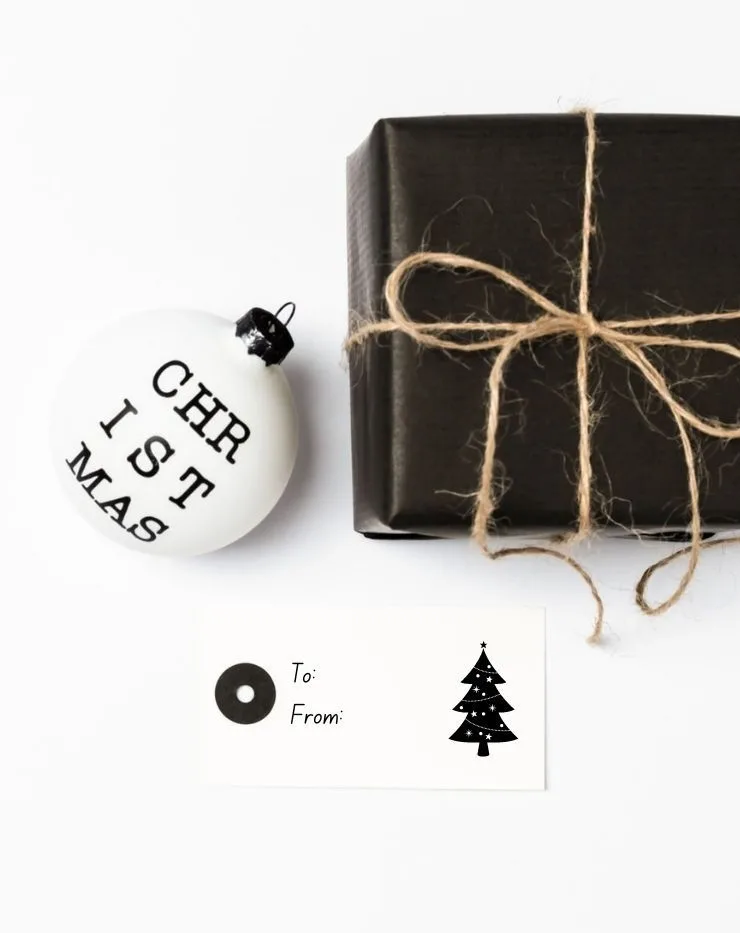 flat lay with a black and white Christmas ornament, black wrapped gift, and a gift tag with a Christmas tree on it