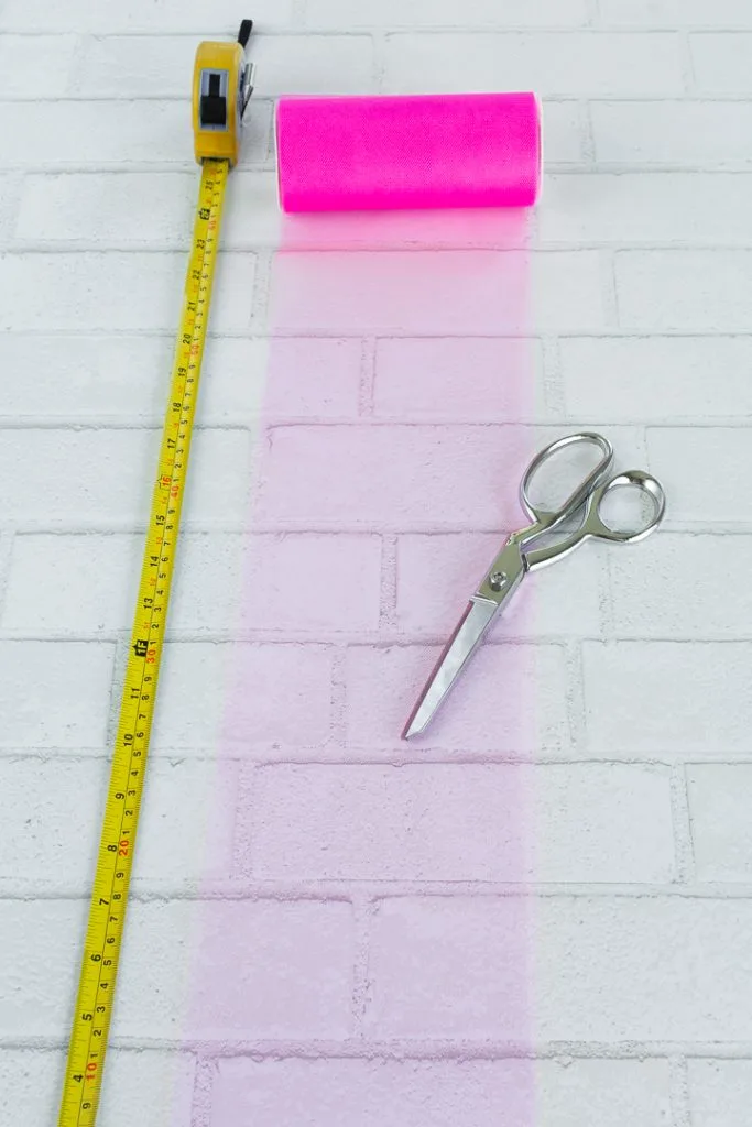 measuring tape, roll of pink tulle, and scissors on a workspace